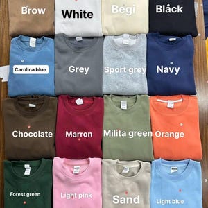 May include: A collection of crewneck sweatshirts in various colors, including brown, white, beige, black, Carolina blue, gray, sport gray, navy, chocolate, maroon, military green, orange, forest green, light pink, sand, and light blue. Each sweatshirt has a label.