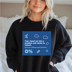 May include: Black sweatshirt with a blue graphic. The graphic includes a sad face, cloud icons, and the text: "Your cloud ran into a problem and needs to restart. We're just collecting some downtime... 0%"