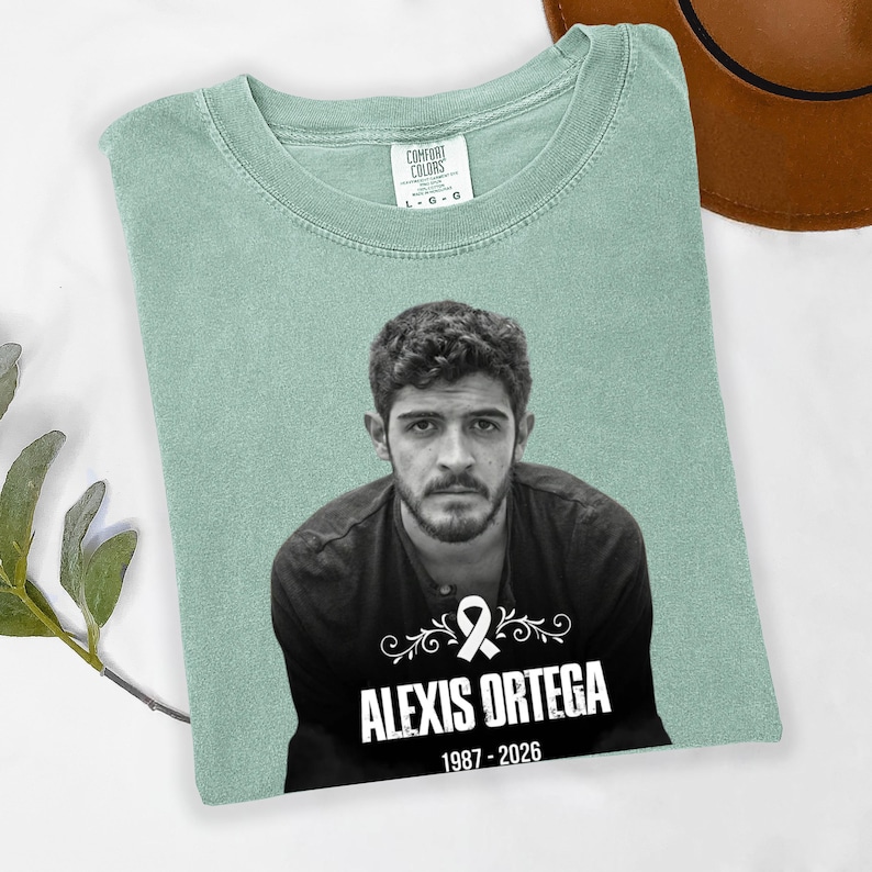 May include: A light green Comfort Colors t-shirt featuring a black and white portrait of a man. The text "ALEXIS ORTEGA 1987-2026" is printed below the portrait, along with a white ribbon graphic.