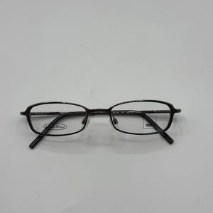 May include: Dark burgundy rectangular spectacles with thin metal frames. The lenses feature a sticker on the left side that reads Spring Hinge and a small rectangular label on the right lens. The inner temple arm displays the text Mz 83 731 48 18 135mm.