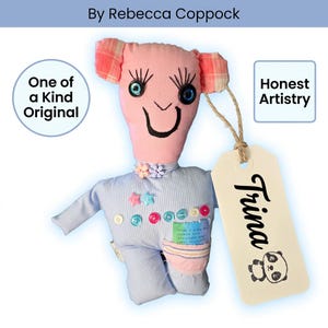 May include: A handmade fabric doll with a pink head, plaid ears, and a blue pinstriped body. It features button eyes with long lashes, a stitched smile, and colorful button accents. A beige tag attached with twine reads Trina with a panda graphic.
