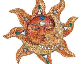 May include: A mosaic sun and moon sculpture with a face on each celestial body. The sun is orange and the moon is yellow, both with closed eyes and kissing. The sculpture is decorated with green, blue, and white accents.