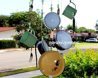 May include: A vintage-style wind chime made from repurposed kitchenware. It features a large yellow enamel lid, smaller enamel lids, mugs, and forks hanging from a metal frame. Green and clear glass beads are strung throughout the chime.