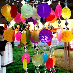 May include: A colorful mobile with round, iridescent, and mirrored ornaments hanging from a white string. The mobile is made of metal and has a circular frame. The ornaments are in various colors, including red, green, blue, purple, yellow, and pink.
