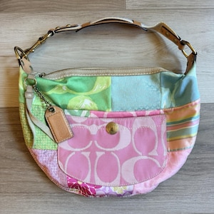 Puede incluir: Un bolso de mano tipo patchwork multicolor con una mezcla de paneles de tela en tonos pastel rosa, verde, azul y amarillo. El bolso incluye un bolsillo frontal con cierre de broche dorado, una etiqueta de cuero beige y una correa de hombro de cuero beige.