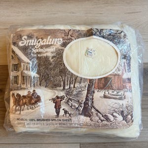 May include: A cream-colored Snugalure Springmaid warm sheet packaged in clear plastic. The packaging features a winter scene with a horse-drawn carriage, a person carrying wood, and a dog. Text includes "Snugalure," "THE WARM SHEET," and "60 X 80 IN."