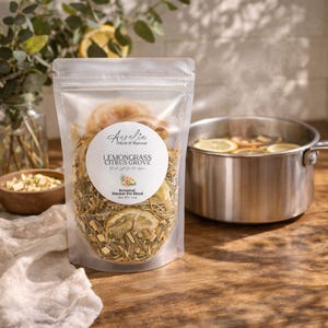 May include: A clear bag of "Lemongrass Citrus Grove" botanical simmer pot blend with dried lemon slices and herbs. A stainless steel pot with lemon slices steams in the background. The label reads "Aurelia Herb & Harvest".