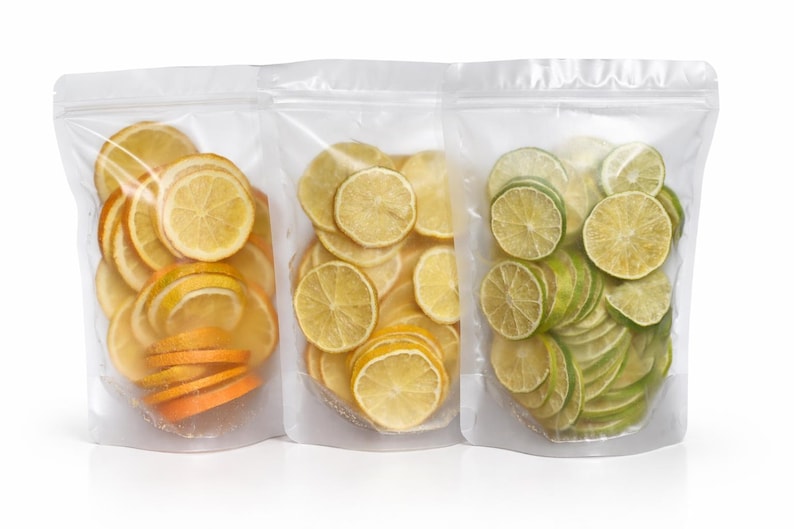May include: Three clear stand-up pouches containing dehydrated fruit slices. The left pouch holds orange slices, the middle pouch contains yellow lemon slices, and the right pouch is filled with green lime slices, all visible through the plastic.
