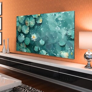 Puede incluir: Una impresión en lienzo rectangular que representa una escena acuática serena con nenúfares y una flor de loto blanca. La obra de arte tiene una paleta de colores verde azulado y verde, con gotas de agua visibles en las hojas. La impresión está montada en una pared encima de un mueble blanco y negro.