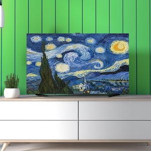 May include: A framed canvas print of Van Gogh's "Starry Night" painting. The artwork features a swirling blue night sky with yellow stars and a prominent cypress tree in the foreground. The print is displayed on a white cabinet.