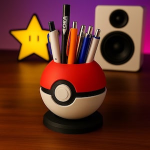May include: A red, white, and black Poké Ball-shaped pen holder containing several pens of different colours. The pen holder is on a black base. A yellow star-shaped light is in the background.