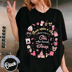 Puede incluir: Camiseta negra con un dise&ntilde;o circular de Disney en rosa y blanco. El texto dice "Once upon a time there was a Girl who loved Disney." La camiseta est&aacute; etiquetada como "Comfort Colors Black."