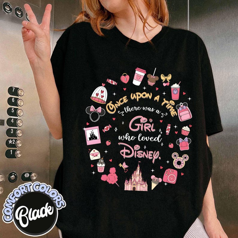Puede incluir: Camiseta negra con un dise&ntilde;o circular de Disney en rosa y blanco. El texto dice "Once upon a time there was a Girl who loved Disney." La camiseta est&aacute; etiquetada como "Comfort Colors Black."