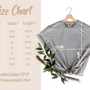 May include: A gray Comfort Colors 1717 adult heavyweight t-shirt hangs on a wooden hanger. The size chart shows measurements in inches for width and length, ranging from S to 4XL.