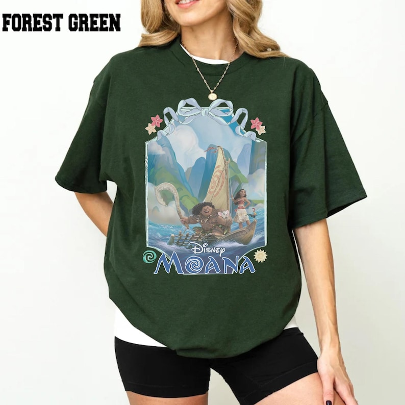 Puede incluir: Una camiseta de manga corta en color verde bosque con un estampado gr&aacute;fico de los personajes de Disney Moana, Maui y Moana, en un barco. El dise&ntilde;o est&aacute; enmarcado por una cinta azul claro e incluye el texto Disney Moana en azul.