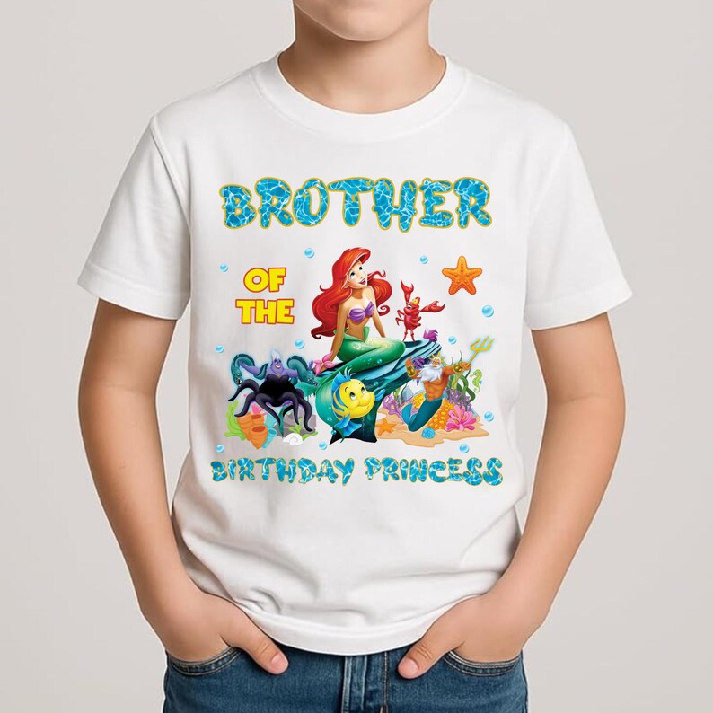 May include: White t-shirt with a colorful graphic featuring Ariel from The Little Mermaid, a lobster, and other sea creatures. Text reads "Brother of the Birthday Princess" in blue and yellow.