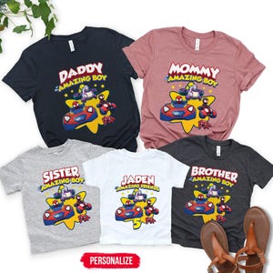 May include: Five short-sleeve t-shirts in navy, mauve, heather gray, white, and charcoal gray. Each shirt features a graphic of cartoon characters in vehicles over a yellow star with text including DADDY, MOMMY, SISTER, BROTHER, and JADEN.