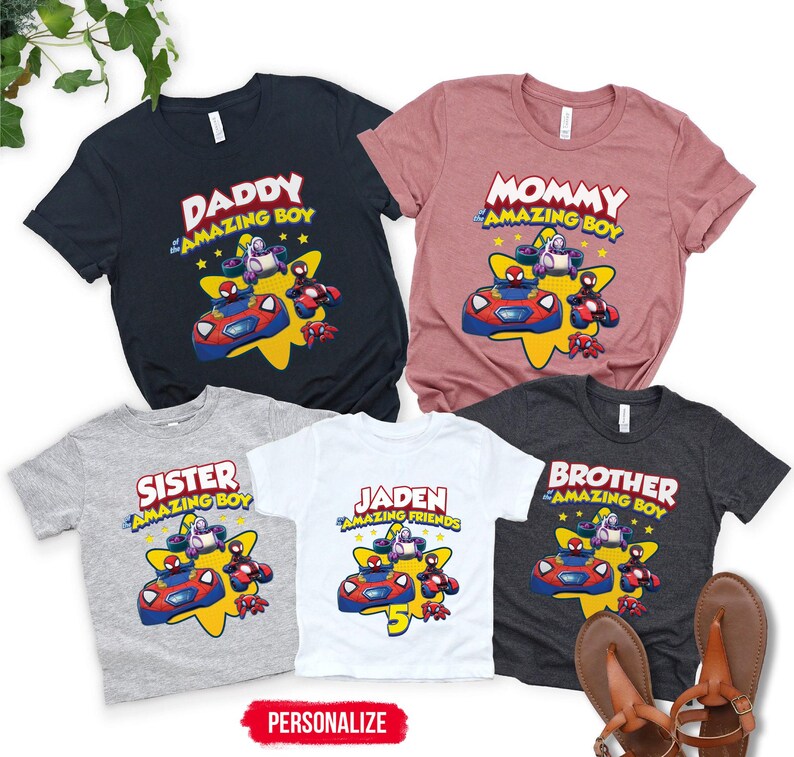 May include: Five short-sleeve t-shirts in navy, mauve, heather gray, white, and charcoal gray. Each shirt features a graphic of cartoon characters in vehicles over a yellow star with text including DADDY, MOMMY, SISTER, BROTHER, and JADEN.