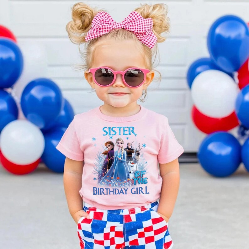 May include: A young child wearing a pink t-shirt with the text "Sister of the Birthday Girl" and a graphic of characters from the movie Frozen. The child is also wearing pink sunglasses and a pink gingham bow. Blue, white, and red balloons are in the background.