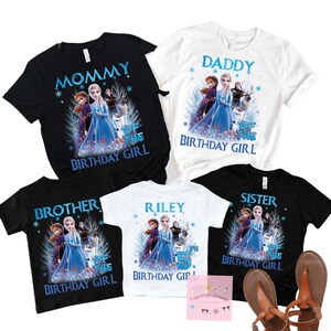 May include: A collection of black and white t-shirts with a Frozen theme. The shirts feature Elsa, Anna, and Olaf, with text such as "Mommy", "Daddy", "Brother", "Sister", and a personalized shirt with the name "Riley" and the number "5".