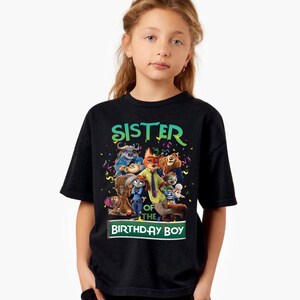Pu&ograve; includere: T-shirt nero con una grafica colorata con personaggi del film Zootropolis. Il testo "SISTER OF THE BIRTHDAY BOY" &egrave; visualizzato in verde e bianco. La maglietta &egrave; indossata da una ragazzina.