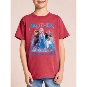 May include: Red t-shirt with the text "BROTHER OF THE BIRTHDAY GIRL" in blue. The shirt features a graphic of characters from the movie Frozen, including Elsa, Anna, Olaf, and Kristoff. The shirt is made of a soft material.