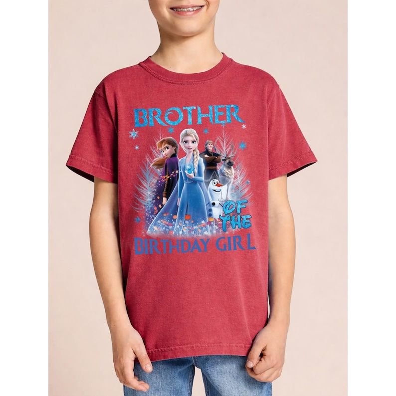 May include: Red t-shirt with the text "BROTHER OF THE BIRTHDAY GIRL" in blue. The shirt features a graphic of characters from the movie Frozen, including Elsa, Anna, Olaf, and Kristoff. The shirt is made of a soft material.