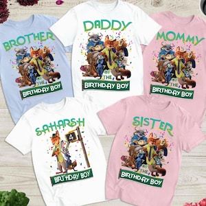Pu&ograve; includere: Cinque magliette colorate con personaggi dei cartoni animati e testo. Le magliette sono azzurre, bianche e rosa. Il testo include "Brother", "Daddy", "Mommy", "Sister" e un nome. Ogni maglietta ha il testo "Birthday Boy".