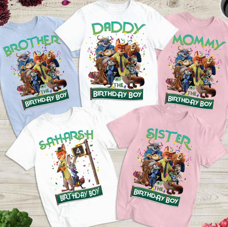 Pu&ograve; includere: Cinque magliette colorate con personaggi dei cartoni animati e testo. Le magliette sono azzurre, bianche e rosa. Il testo include "Brother", "Daddy", "Mommy", "Sister" e un nome. Ogni maglietta ha il testo "Birthday Boy".