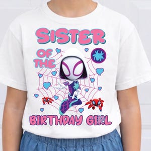 Puede incluir: Camiseta blanca con un dise&ntilde;o de dibujos animados de Spider-Gwen y el texto "SISTER OF THE BIRTHDAY GIRL" en rosa y azul. El dise&ntilde;o incluye corazones, telara&ntilde;as y gr&aacute;ficos de ara&ntilde;as.