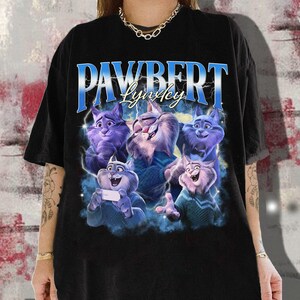 Op de afbeelding: Zwart t-shirt met een afbeelding van cartoonkatten en de tekst "PAWBERT Lynkey" in blauw en wit. De katten zijn in tinten paars, blauw en wit. Het shirt heeft een casual stijl.
