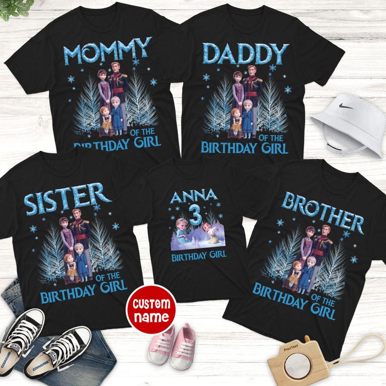 May include: Black t-shirts with a Frozen theme. The shirts have the words "MOMMY", "DADDY", "SISTER", "ANNA 3", and "BROTHER" in blue text. Each shirt features a graphic of characters from the movie and the phrase "OF THE BIRTHDAY GIRL".