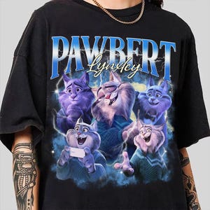 Op de afbeelding: Zwart T-shirt met een cartoonillustratie van verschillende blauwe katten met verschillende uitdrukkingen. De tekst "PAWBERT Lynkley" staat in blauw en wit boven de katten gedrukt. Bliksemflitsen zijn op de achtergrond.