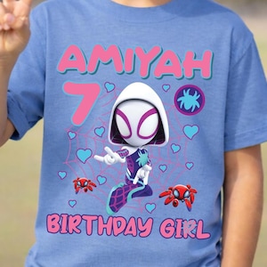 Puede incluir: Camiseta azul claro con un gr&aacute;fico de Spider-Gwen, el nombre "Amiyah" y el n&uacute;mero "7" en rosa. Tambi&eacute;n se muestran las palabras "BIRTHDAY GIRL". El dise&ntilde;o incluye corazones y elementos de telara&ntilde;a.