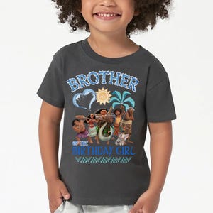 Peut inclure: Un t-shirt gris fonc&eacute; &agrave; manches courtes avec une impression graphique portant le texte BROTHER OF THE BIRTHDAY GIRL en bleu. Le motif comprend des illustrations de personnages du film Moana, un soleil, un palmier et une vague en forme de c&oelig;ur.