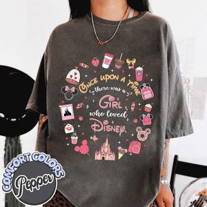 Puede incluir: Camiseta Comfort Colors gris oscuro con un gr&aacute;fico circular. El gr&aacute;fico dice: "Once upon a time there was a girl who loved Disney." El dise&ntilde;o incluye iconos de Disney en rosa y blanco.