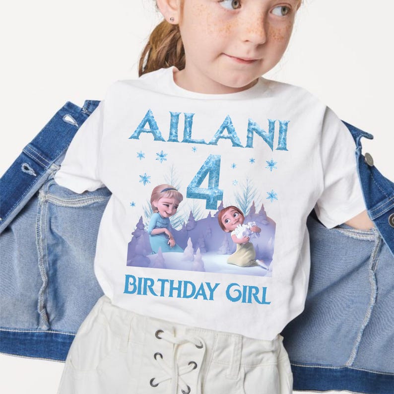 May include: White t-shirt with a blue graphic. The graphic includes the name "Ailani", the number "4", and the words "BIRTHDAY GIRL". The design also features illustrations of two animated characters in a winter scene.