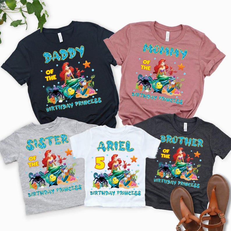 May include: Five short-sleeved t-shirts with colorful graphics. The shirts are navy, mauve, gray, white, and charcoal. Each shirt features a mermaid design with text that reads "Daddy", "Mummy", "Sister", "Ariel 5", and "Brother" with "Birthday Princess".