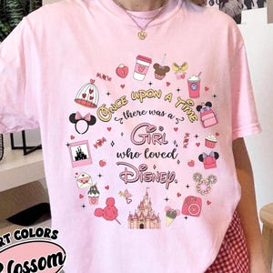 Puede incluir: Camiseta rosa claro con un dise&ntilde;o de Disney. El dise&ntilde;o incluye un castillo, orejas de Minnie Mouse y el texto "Once Upon a Time there was a Girl who loved Disney."