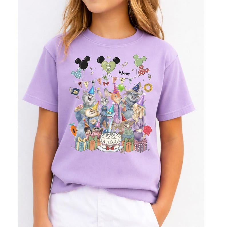 Pu&ograve; includere: Una maglietta lilla con un design per feste di compleanno con personaggi dei cartoni animati, palloncini e una torta. Il design include la parola "Name" e il numero "3". La maglietta &egrave; a maniche corte e girocollo.
