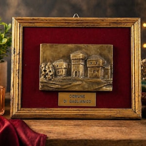 Könnte beinhalten: Gerahmte Bronzereliefskulptur, die eine Stadtszene darstellt, vor rotem Samthintergrund. Der Rahmen ist goldfarben. Eine kleine Plakette unten lautet "COMUNE DI GAGLIANICO".