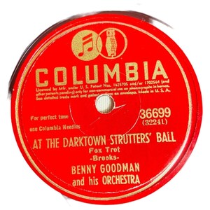 May include: A round red vinyl phonograph record label featuring gold text. The label displays the Columbia logo, the song title At the Darktown Strutters' Ball, the artist Benny Goodman and his Orchestra, and the catalog number 36699.