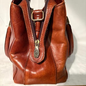 Peut inclure: Sac &agrave; main en cuir marron avec fermeture &eacute;clair et tirette en m&eacute;tal. Le sac a une poign&eacute;e sup&eacute;rieure et deux poches lat&eacute;rales. Le sac mesure environ 25 cm de large.
