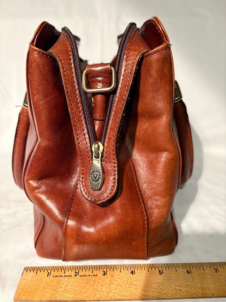 Peut inclure: Sac &agrave; main en cuir marron avec fermeture &eacute;clair et tirette en m&eacute;tal. Le sac a une poign&eacute;e sup&eacute;rieure et deux poches lat&eacute;rales. Le sac mesure environ 25 cm de large.