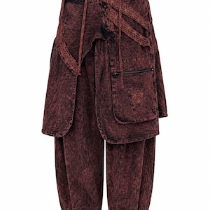 May include: Dark burgundy acid-wash trousers featuring a layered wrap-style waist with button closures, adjustable straps with a geometric pattern, a zippered pocket on the front, and elasticated cuffs at the bottom of the tapered legs.