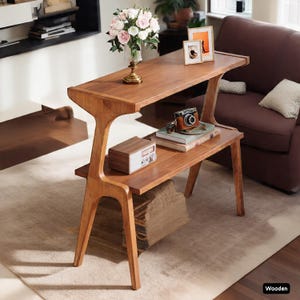 May include: A two-tiered wooden side table with a warm, natural finish. The table features a unique, curved leg design and holds decorative items like a camera, books, and a vase of flowers. The table is approximately 30 inches long.