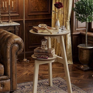 May include: A small, two-tiered side table with a light wood finish. The top tier holds a magnifying glass, books, and a vase with a red rose. The lower tier displays books, a small clock, and eyeglasses. The table is set on a patterned rug.