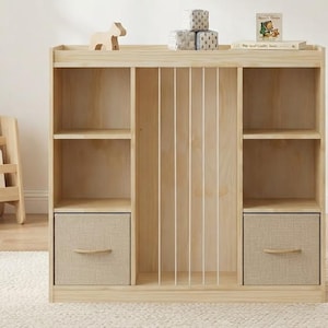 May include: A light-colored wooden storage unit featuring two side sections with open shelves and fabric drawers, and a central vertical compartment with white dowel dividers. The unit has a flat top surface for display and a natural wood grain finish.