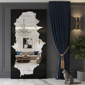 May include: A large, black-framed mirror with an irregular, organic-shaped cutout, revealing a glimpse of a luxurious living room. The mirror reflects a chandelier, artwork, and a beige sofa. A blue curtain and a potted plant are on the right.