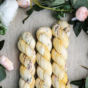 Puede incluir: Tres ovillos de hilo amarillo con motas blancas y verdes. El hilo está dispuesto en espiral.